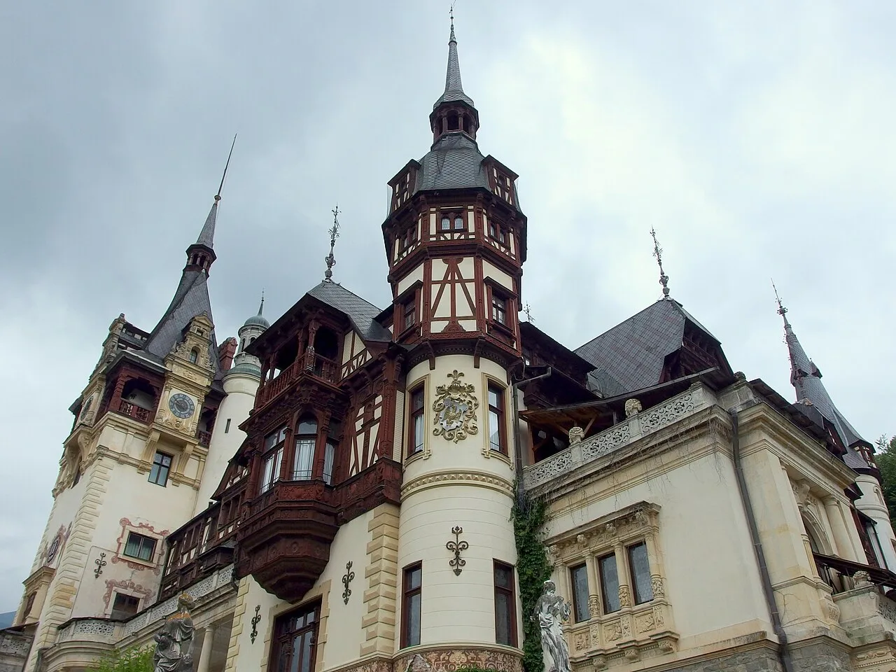 The ornate Neo-Renaissance facade of Peles Castle near Sinaia, timber-framed towers and spires against a grey Carpathian sky