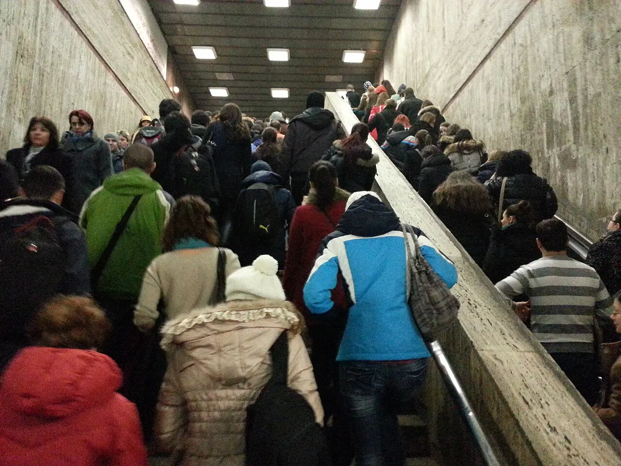 A dense crowd of commuters packed onto a staircase at a Bucharest metro station during rush hour, many carrying bags and backpacks