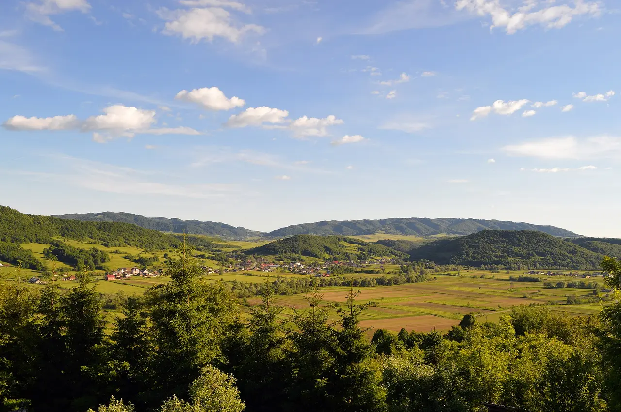 Rolling green hills, hay meadows and scattered farmhouses in the Maramures countryside under a wide sky