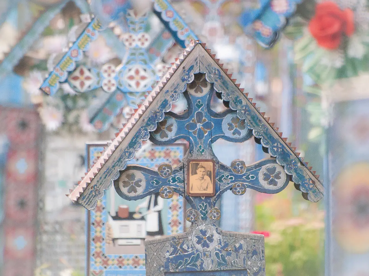 A single blue cross at the Merry Cemetery painted with a small portrait scene and a carved verse in Romanian