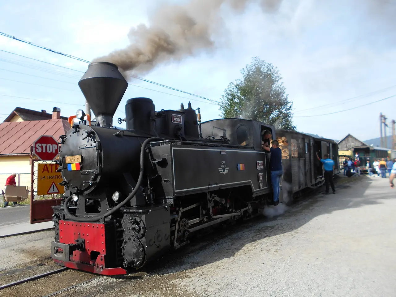 A green steam locomotive of the Mocanita narrow-gauge railway at Viseu de Sus, smoke rising, passengers boarding open carriages