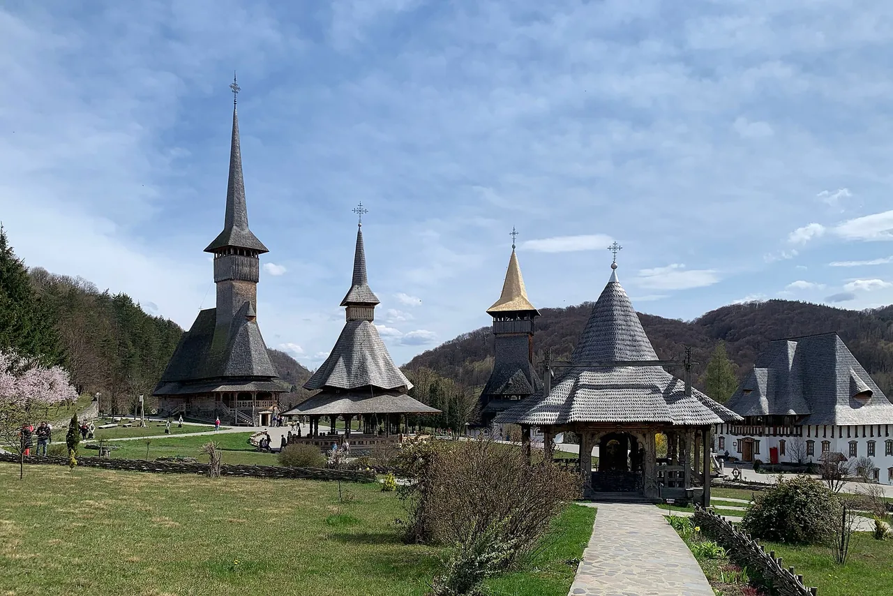 The tall shingled wooden spires of Barsana Monastery rising above green gardens in a Maramures valley