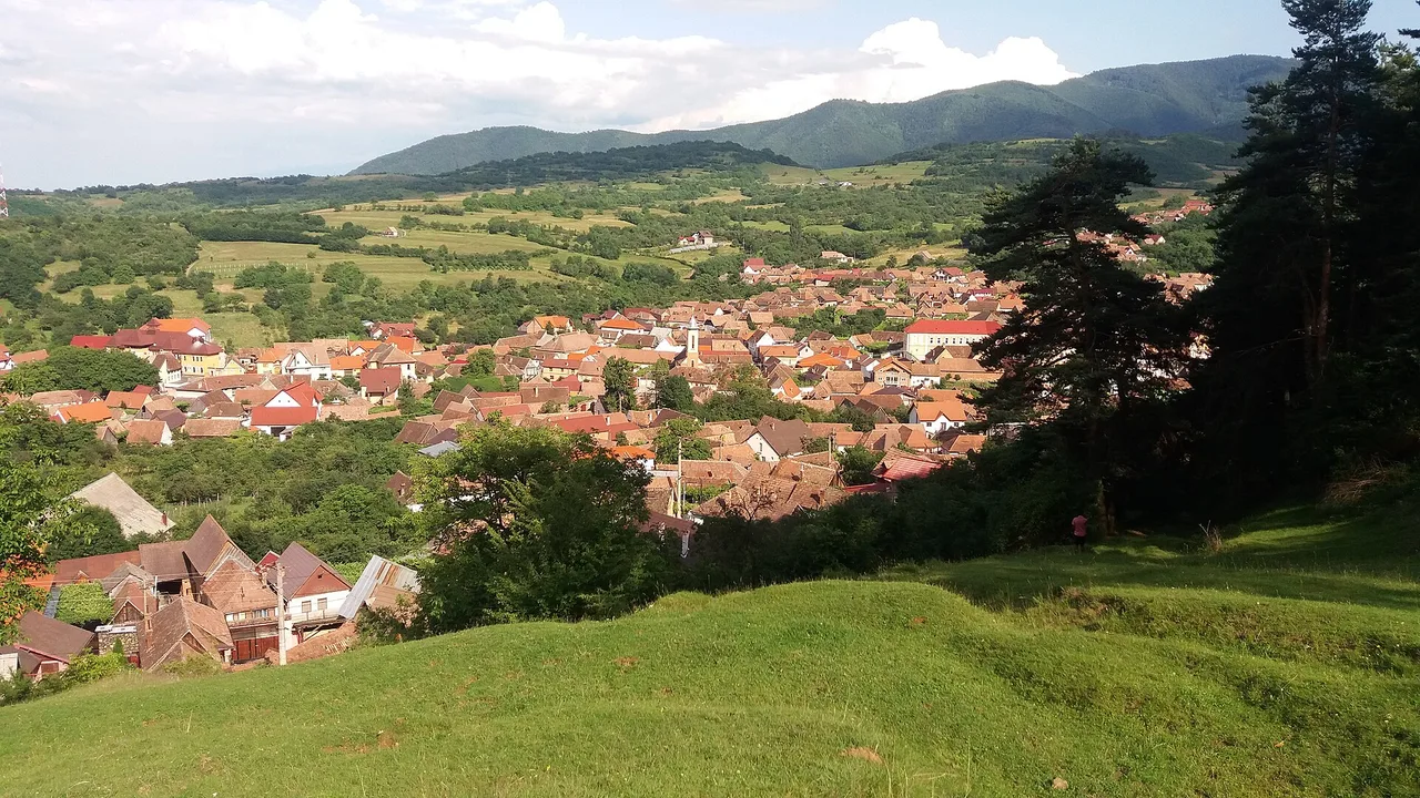 Rasinari village spread across a green hillside below the Cindrel Mountains, red roofs and church towers under a clear sky
