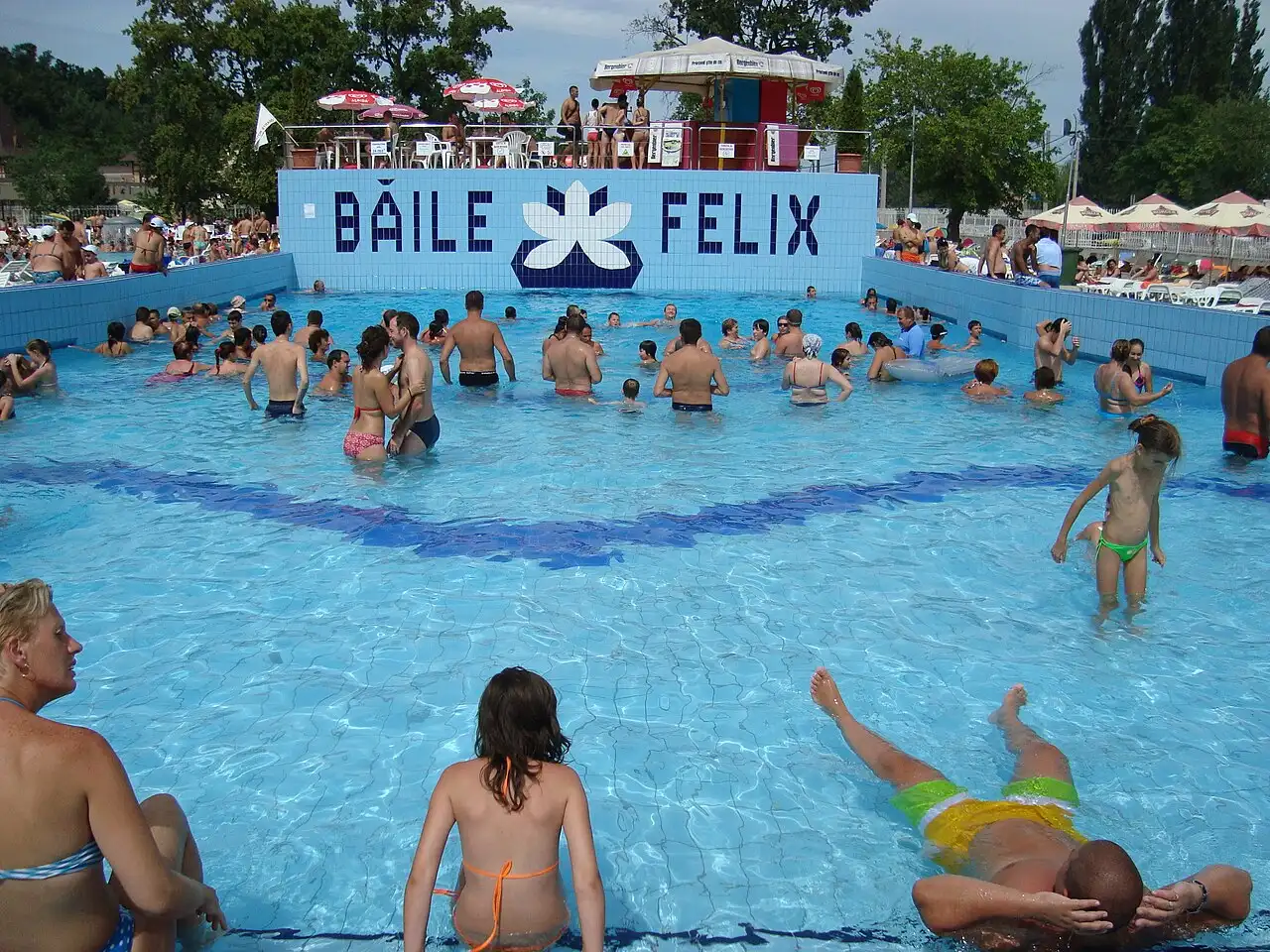 Outdoor thermal pools and bathers at Baile Felix spa resort near Oradea, low buildings and greenery around the water