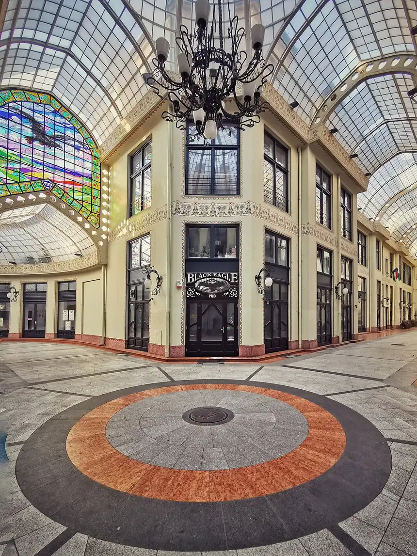 Inside the glazed arcade of the Black Eagle Palace, an ornate covered passage with a glass roof and the stained-glass eagle panel above