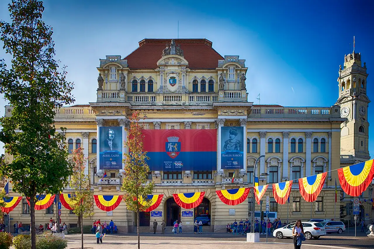 The City Hall Palace of Oradea with its tall clock tower flying the Romanian tricolour, on the bank of the Crisul Repede