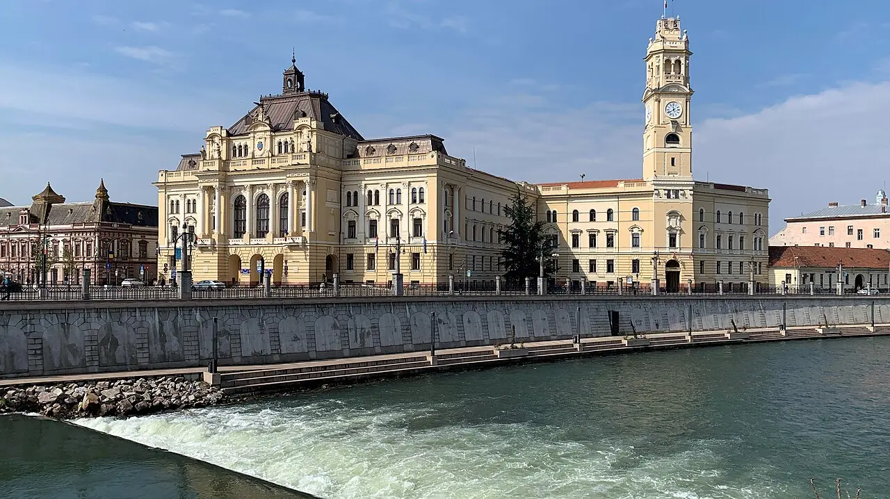 The City Hall Palace of Oradea and its tower reflected in the Crisul Repede river on a bright day, the restored Belle Epoque waterfront behind