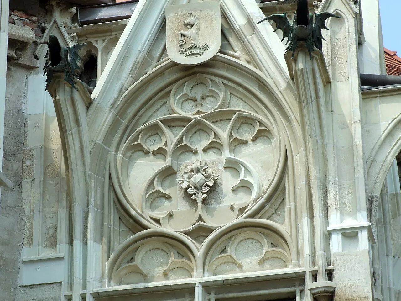 A carved Gothic rose window at Corvin Castle with the family coat of arms showing a raven above it