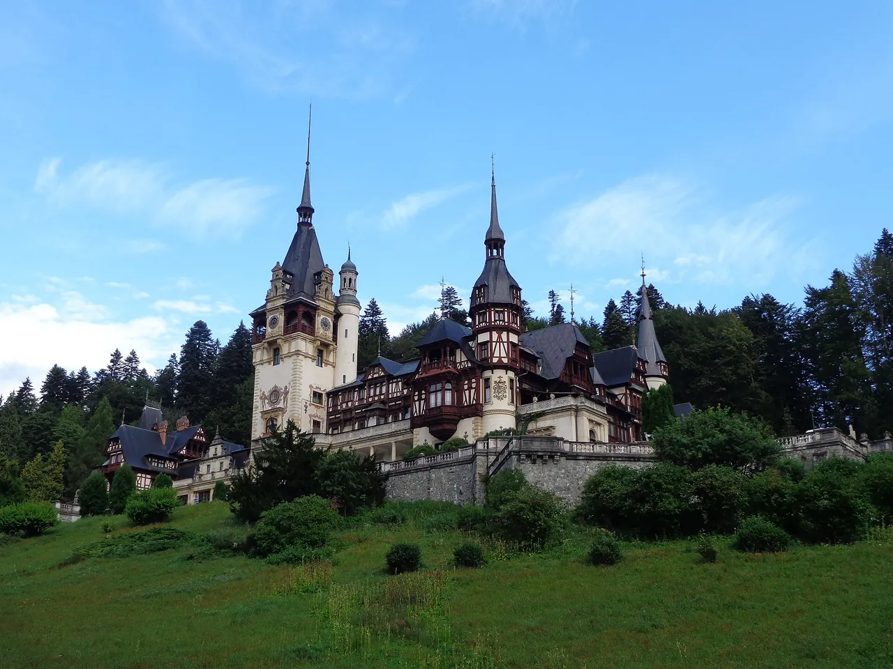 Peles Castle in Sinaia seen from the meadow below, its spires and half-timbered gables against forested hills