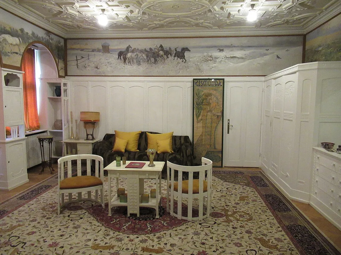 A white-panelled Art Nouveau salon in Pelisor with a painted frieze of horses, pale furniture with yellow cushions and a moulded ceiling