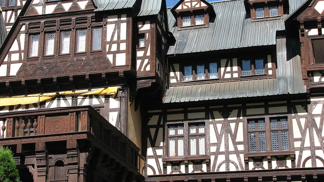 Close-up of the timber framing and carved balcony of Pelisor, dark beams against pale plaster with leaded window panes