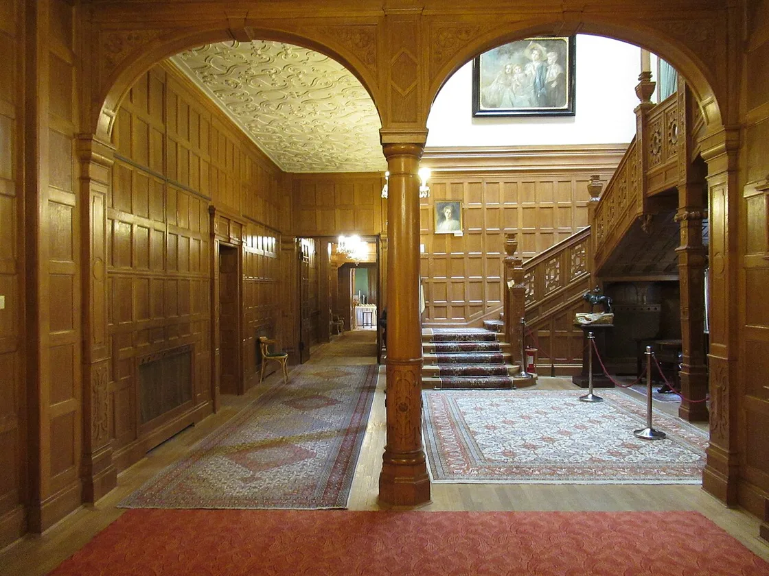 An oak-panelled interior in Pelisor, columns and arches around a carved staircase, oriental rugs on the parquet