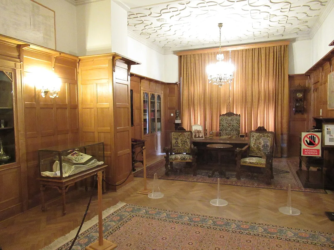 A panelled working room inside Pelisor with a small round table, high-backed embroidered chairs, a display case and a wall clock