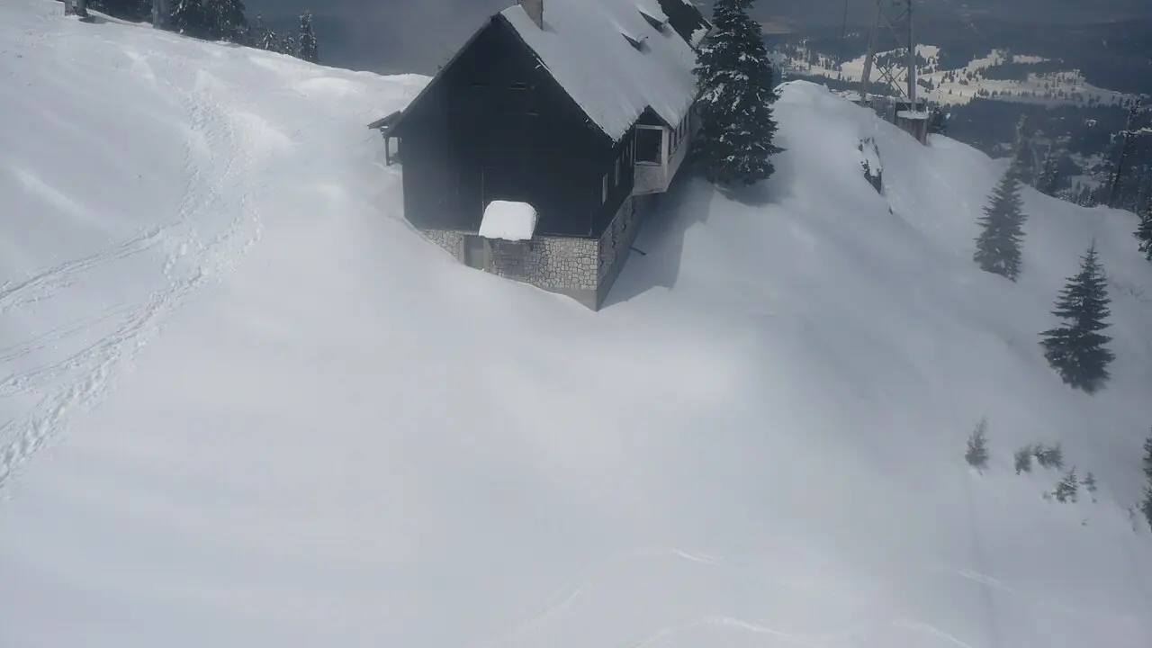 Cabana Postavaru, a dark mountain chalet near the summit, half-buried in deep snow with a lift pylon and the slopes falling away behind