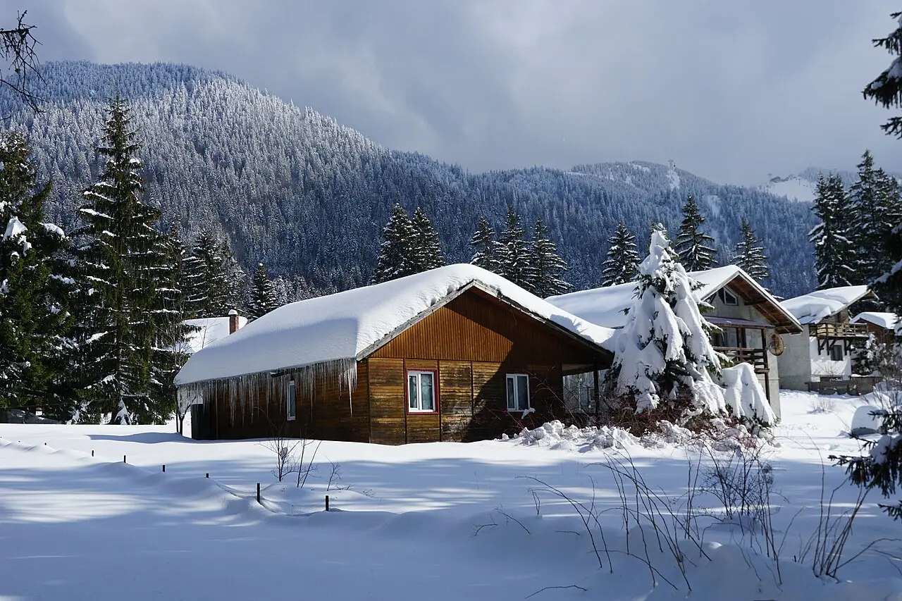 Wooden chalets in Poiana Brasov buried under fresh snow, icicles hanging from the eaves, the forested slopes of Postavaru rising behind