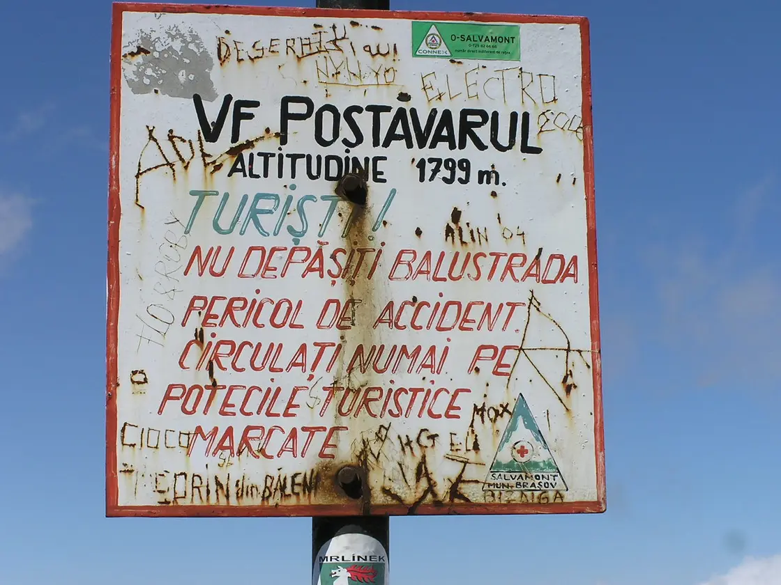A weathered summit sign reading Vf. Postavarul, altitudine 1799 m, against a blue sky