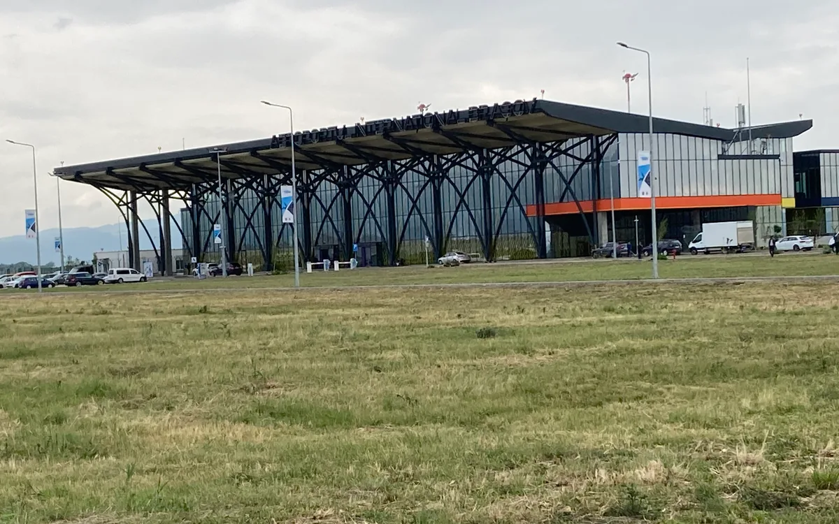 The glass and steel terminal of Brasov-Ghimbav International Airport with its car park, seen across the grass
