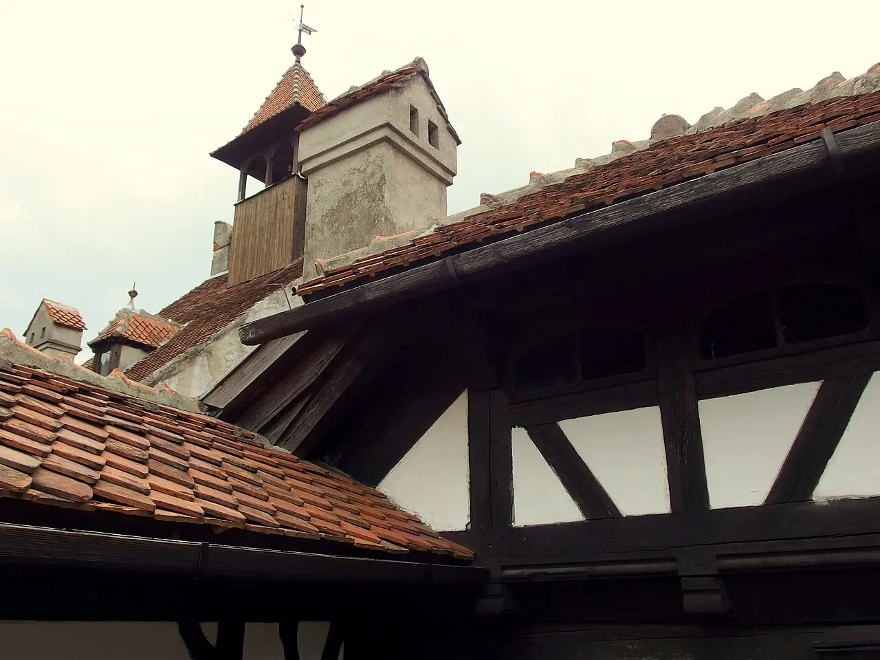 A close view of Bran Castle's steep red-tiled roofs, timber gables and a small tower against a pale sky