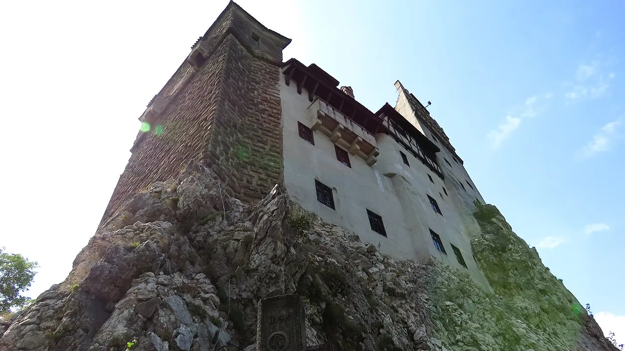 Bran Castle rising white and sheer on its rocky outcrop against a blue sky, seen from directly below