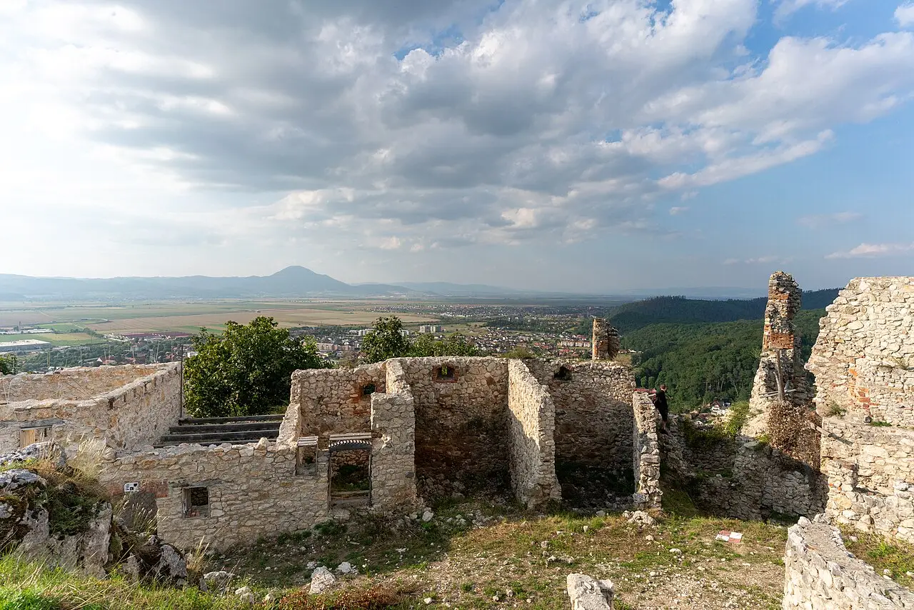 The stone ruins of Rasnov Citadel on its hilltop, walls and a bastion in the foreground and the town of Rasnov and the Barsa plain spread out far below