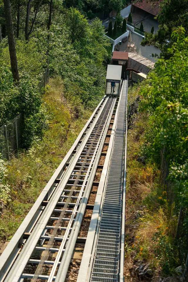 The steep funicular railway track of Rasnov Citadel running down the wooded hillside, the small funicular car near the lower station among the trees and houses