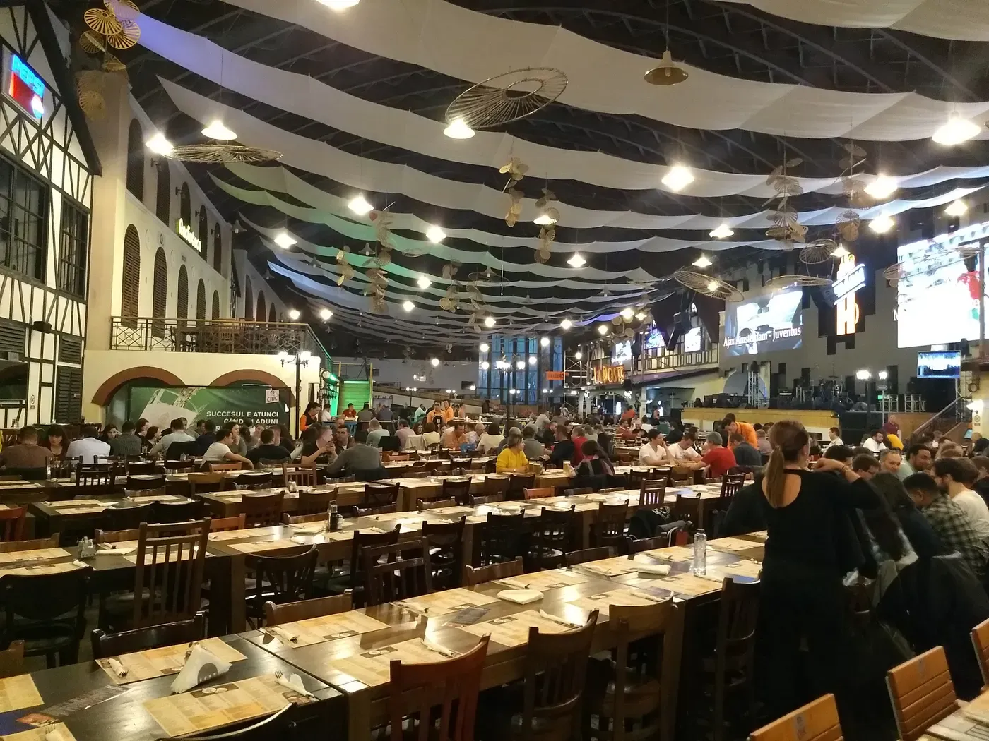 The vast covered hall of Berăria H in Bucharest seen from above, rows of long tables under white canopy drapes and hanging lamps