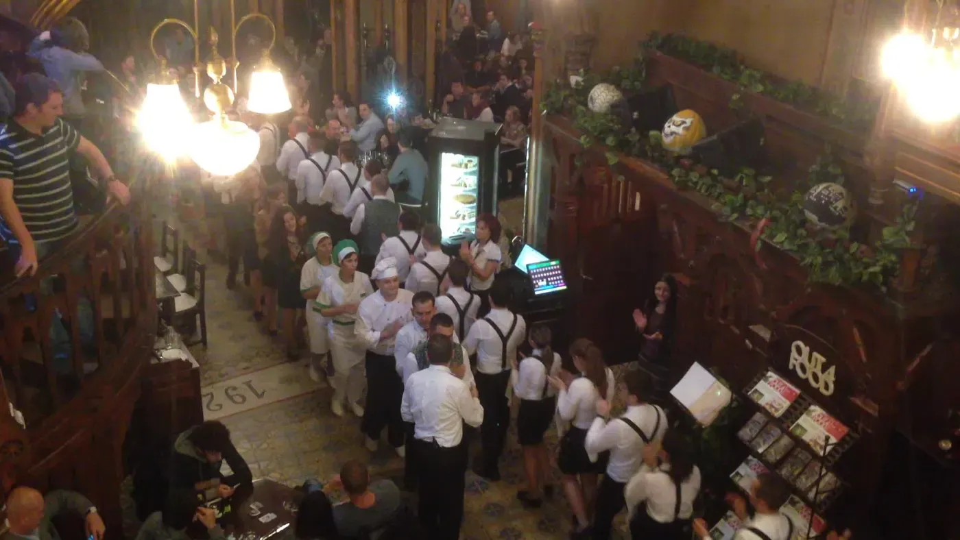 Overhead view of Caru' cu Bere's Gothic-Revival dining hall in Bucharest, staff in folk costume parading between the tables