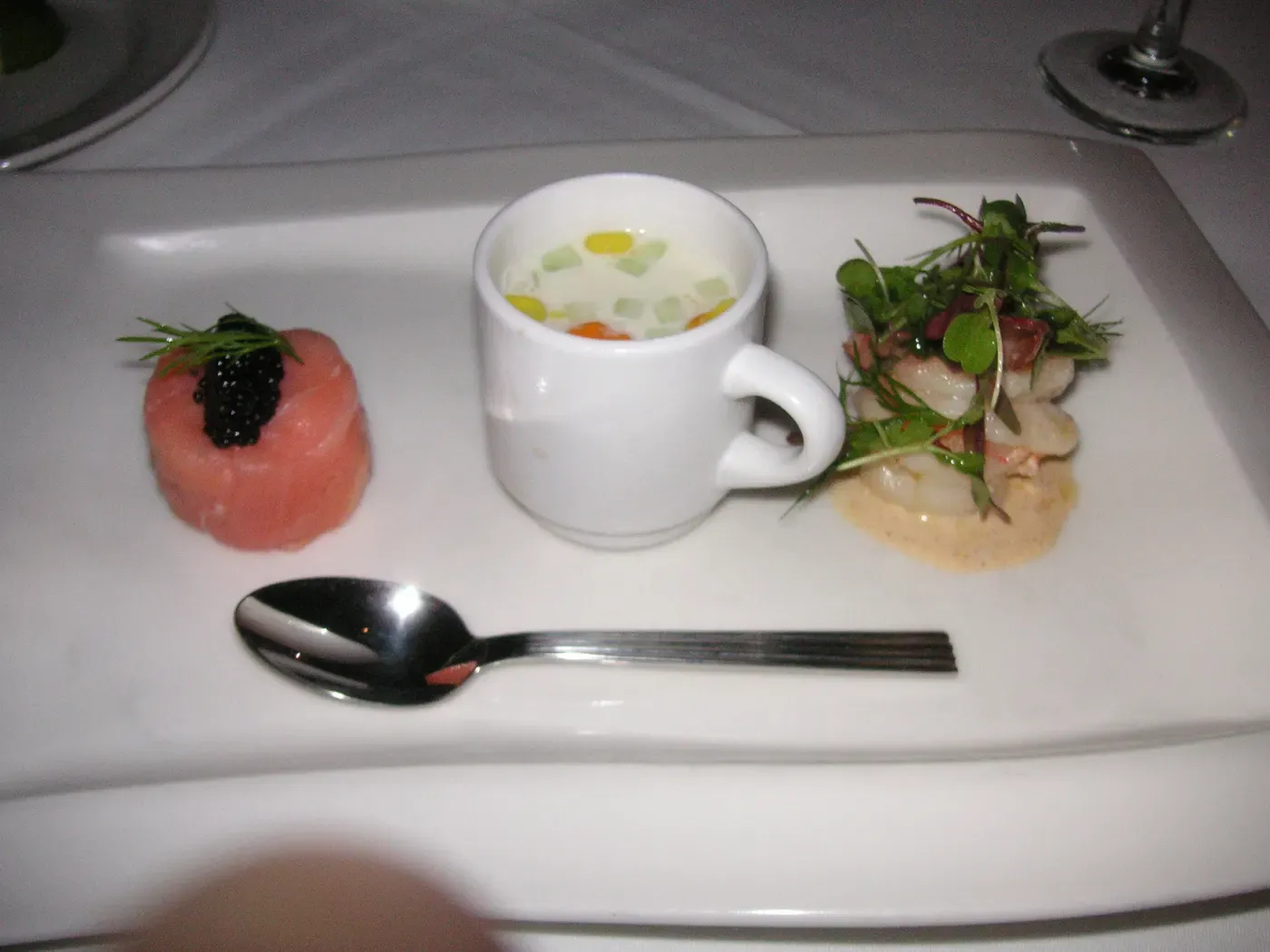 A three-part tasting plate with tuna tartare and caviar, a warm soup in a small cup, and a herb-topped seafood starter, plating typical of a modern multi-course tasting menu