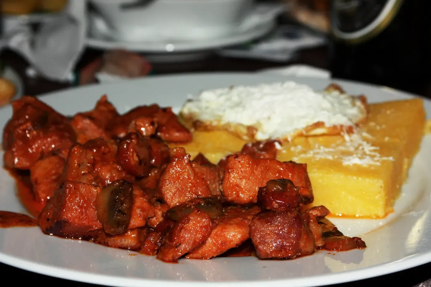 A plate of Romanian tochitură, fried pork pieces with mămăligă polenta and a spoon of soft cheese