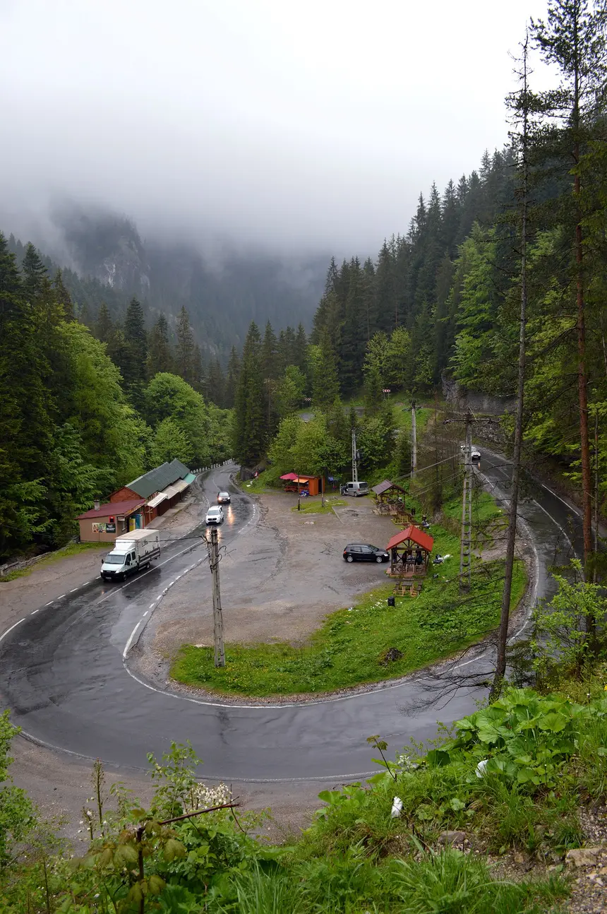 A hairpin bend in the Bicaz Canyon with parked cars and forested cliffs rising into low cloud