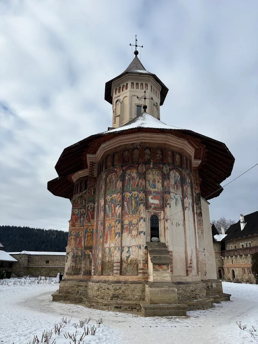 Moldovita Monastery church covered in faded exterior frescoes, with snow on the ground