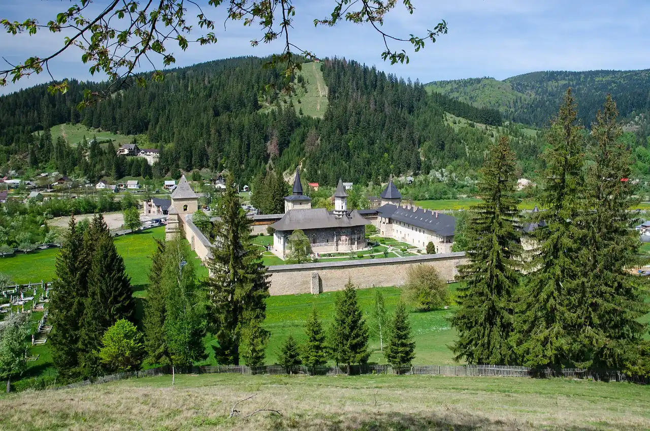 Sucevita Monastery, a fortified painted monastery with corner towers and a shingled church, set among green hills in Bucovina