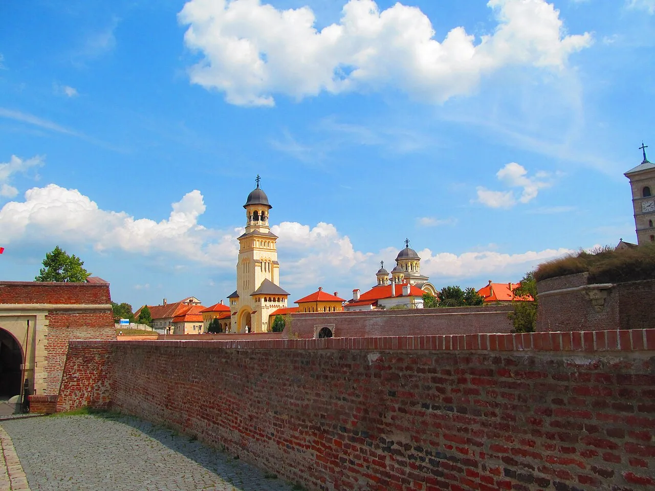 The red-brick ramparts and a gate of the Alba Carolina Citadel in Alba Iulia, with the tall bell tower of the Coronation Cathedral rising inside the walls