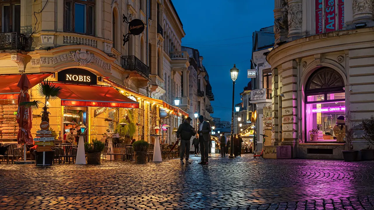 Bucharest's Old Town at blue hour, cobbled Lipscani streets lined with lit cafe terraces where remote workers spend their evenings