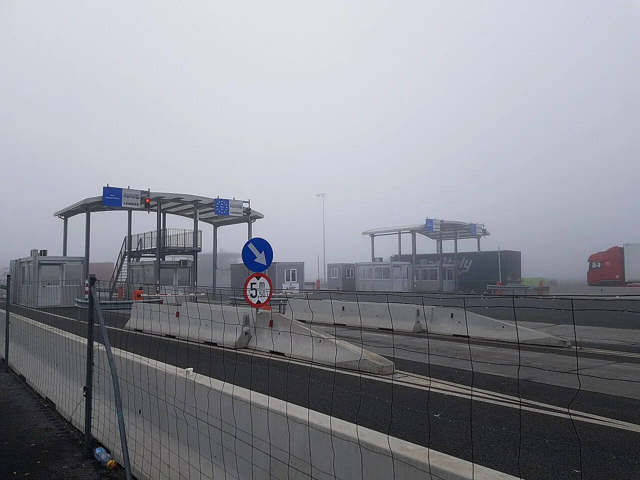 The Nadlac-Nagylak highway border crossing between Romania and Hungary on a foggy day, with empty passport-control booths marked All passports and Lorries, concrete barriers and no queue