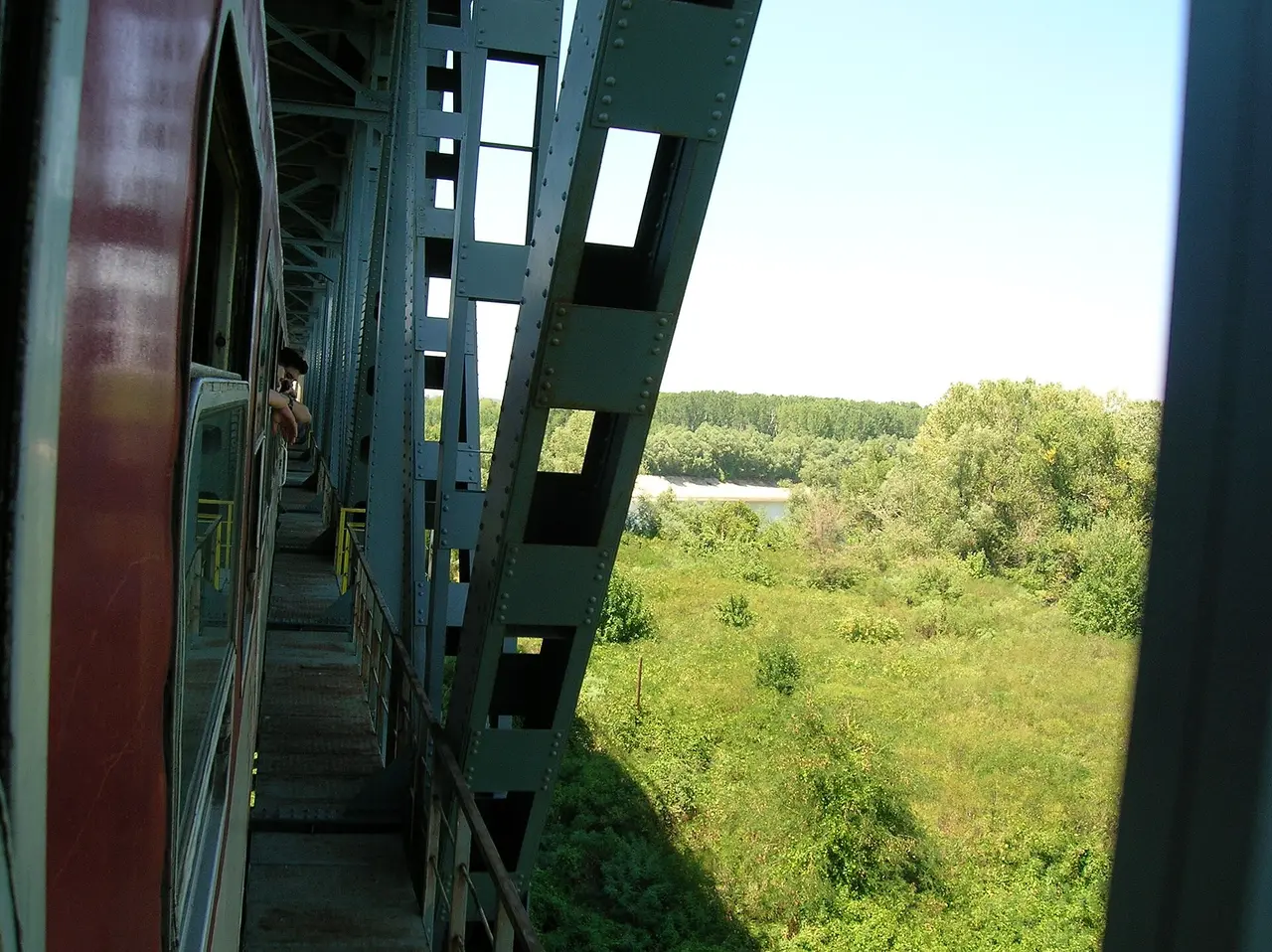 A passenger train crossing a steel railway bridge over the Danube at the Romania-Bulgaria border, with green riverbanks below