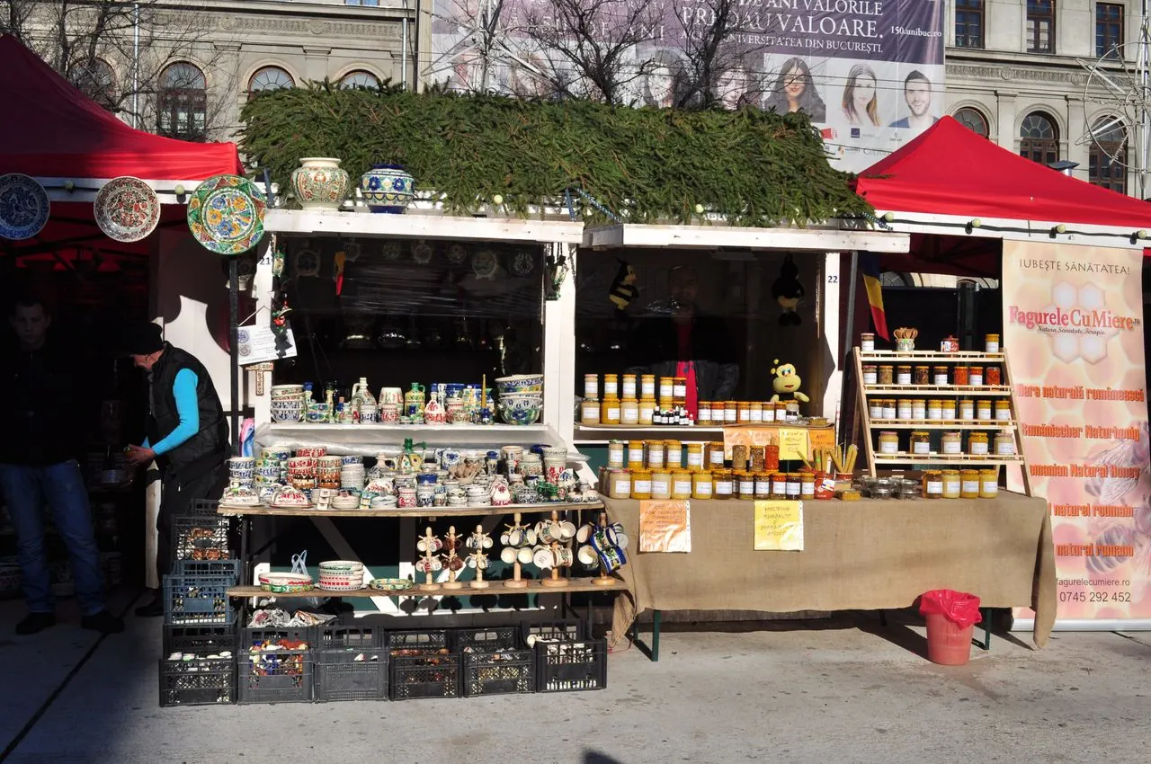 A wooden chalet at the Bucharest Christmas market selling painted ceramics and jars of Romanian honey, spruce branches on the roof