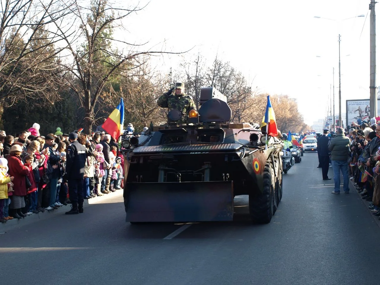 An armoured vehicle rolling past crowds waving Romanian tricolour flags during a National Day parade on 1 December