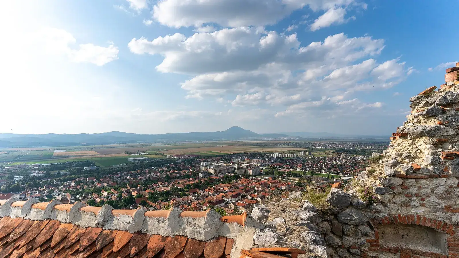 The town of Rasnov and the Barsa plain seen over a tiled citadel roof from the walls above, with the Carpathian foothills on the horizon