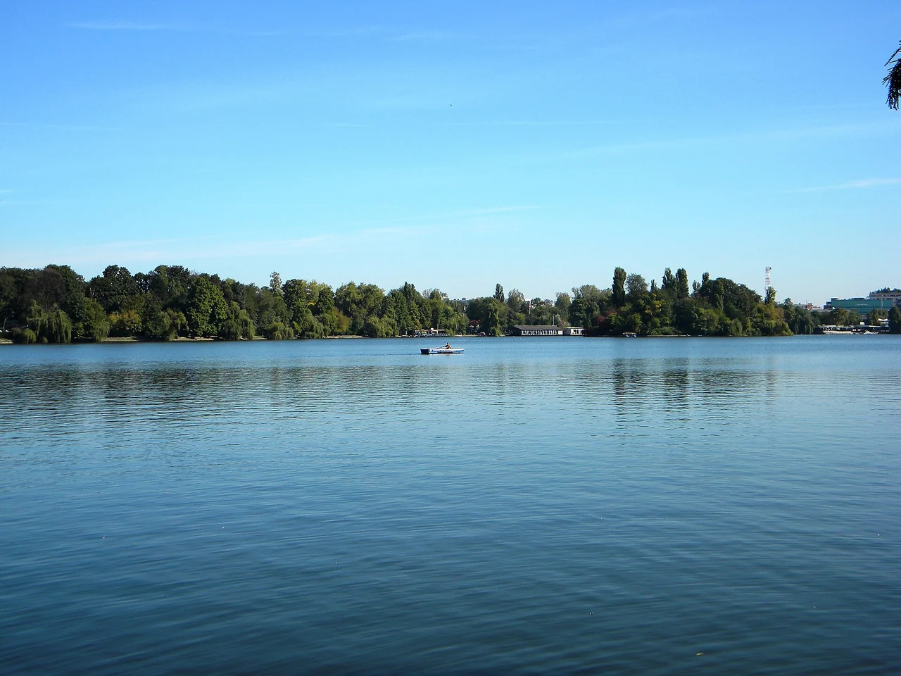 A small rowing boat on the calm water of Lake Herastrau in Bucharest with wooded banks behind it