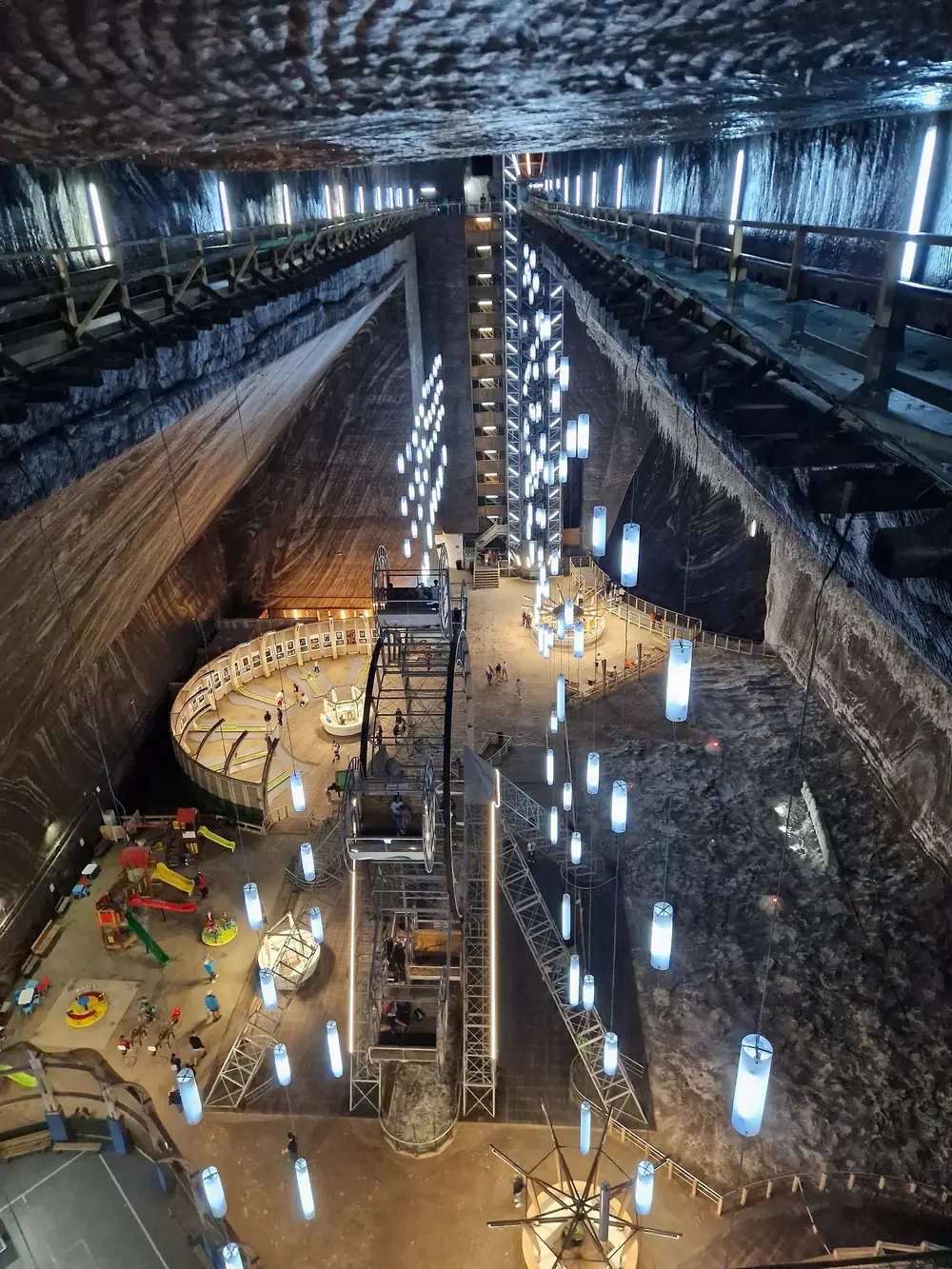 The Rudolf chamber of Salina Turda from the upper gallery, with a coloured childrens playground, a panorama wheel and hanging light tubes on the mine floor