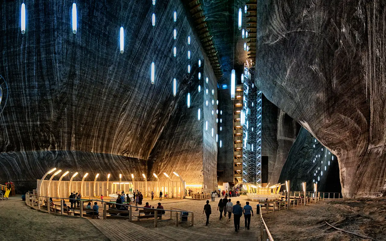 The vast Rudolf chamber of Salina Turda, its striped salt walls hung with glowing light tubes above the amphitheatre and glass lift tower