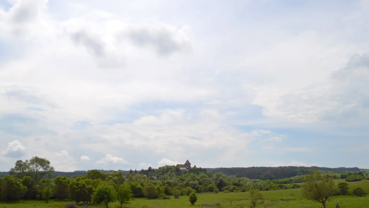 A country road running toward the whitewashed fortified church and red roofs of Viscri, seen from the DJ104L