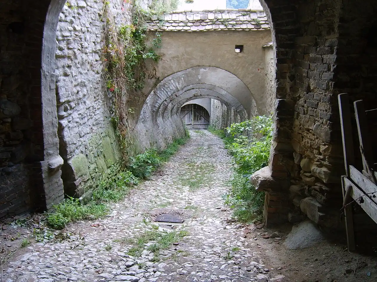 A vaulted covered passage of old stone climbing between the defensive walls of Biertan fortified church, cobbles underfoot