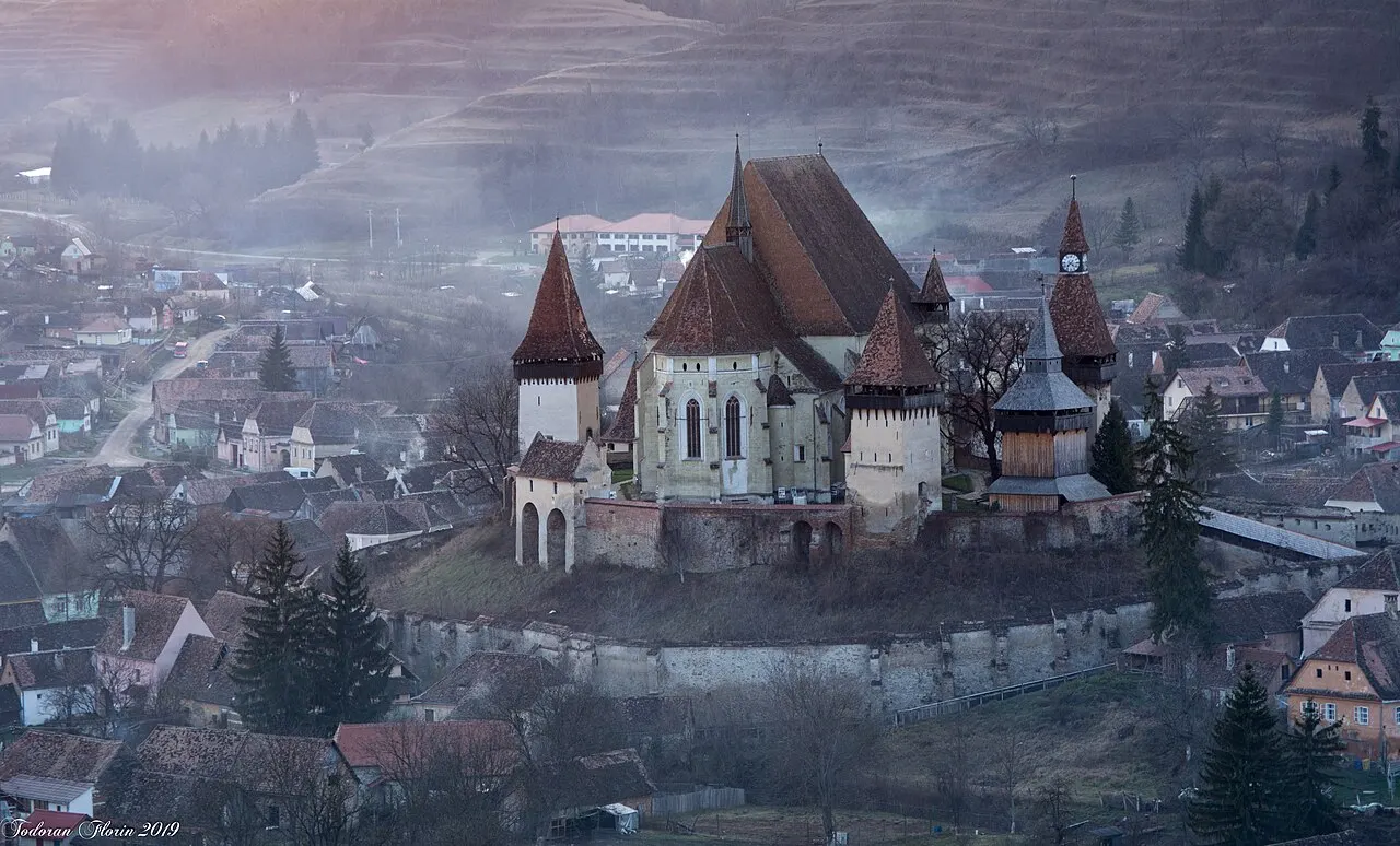 The fortified church of Biertan on its hill ringed by defensive walls and towers, the red-roofed Saxon village around it in morning mist