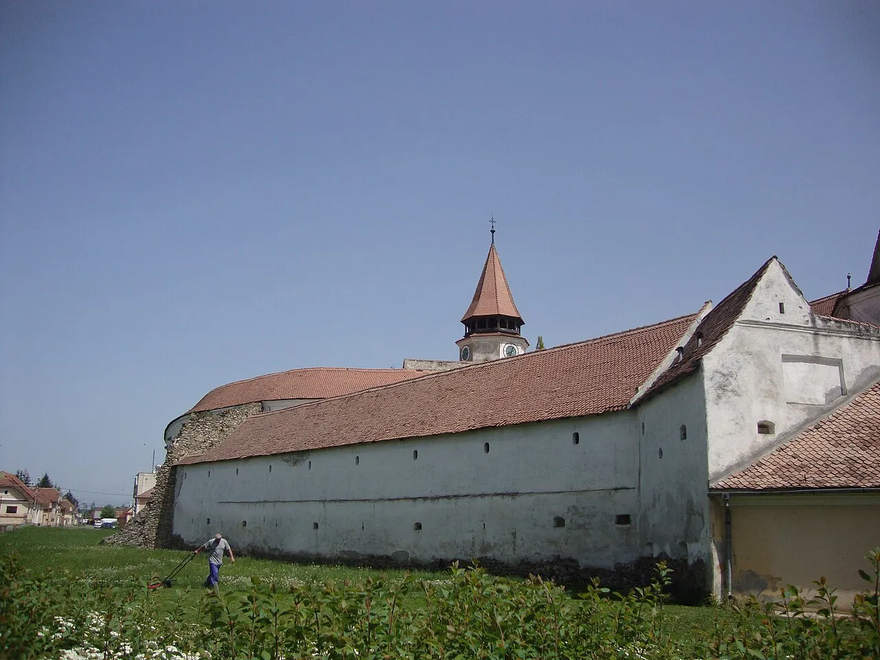 The long curved whitewashed outer wall of Prejmer fortified church with its red tiled roof and clock tower rising behind