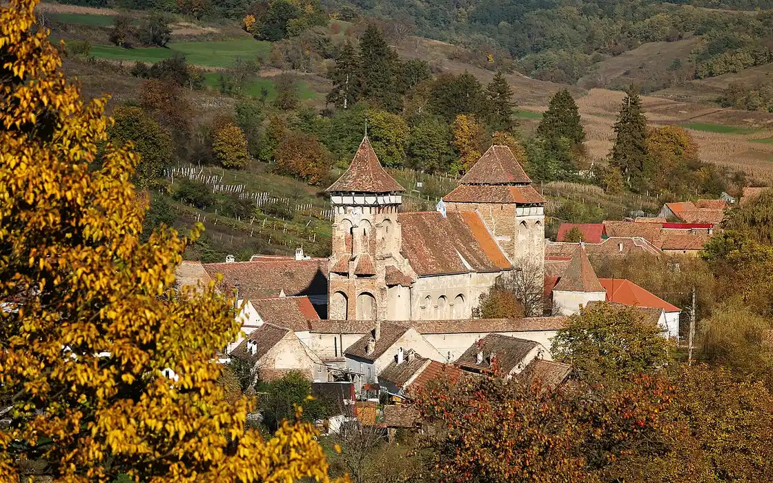 The fortified church of Valea Viilor behind its ring of whitewashed defensive walls and a gate tower, wooded hills behind