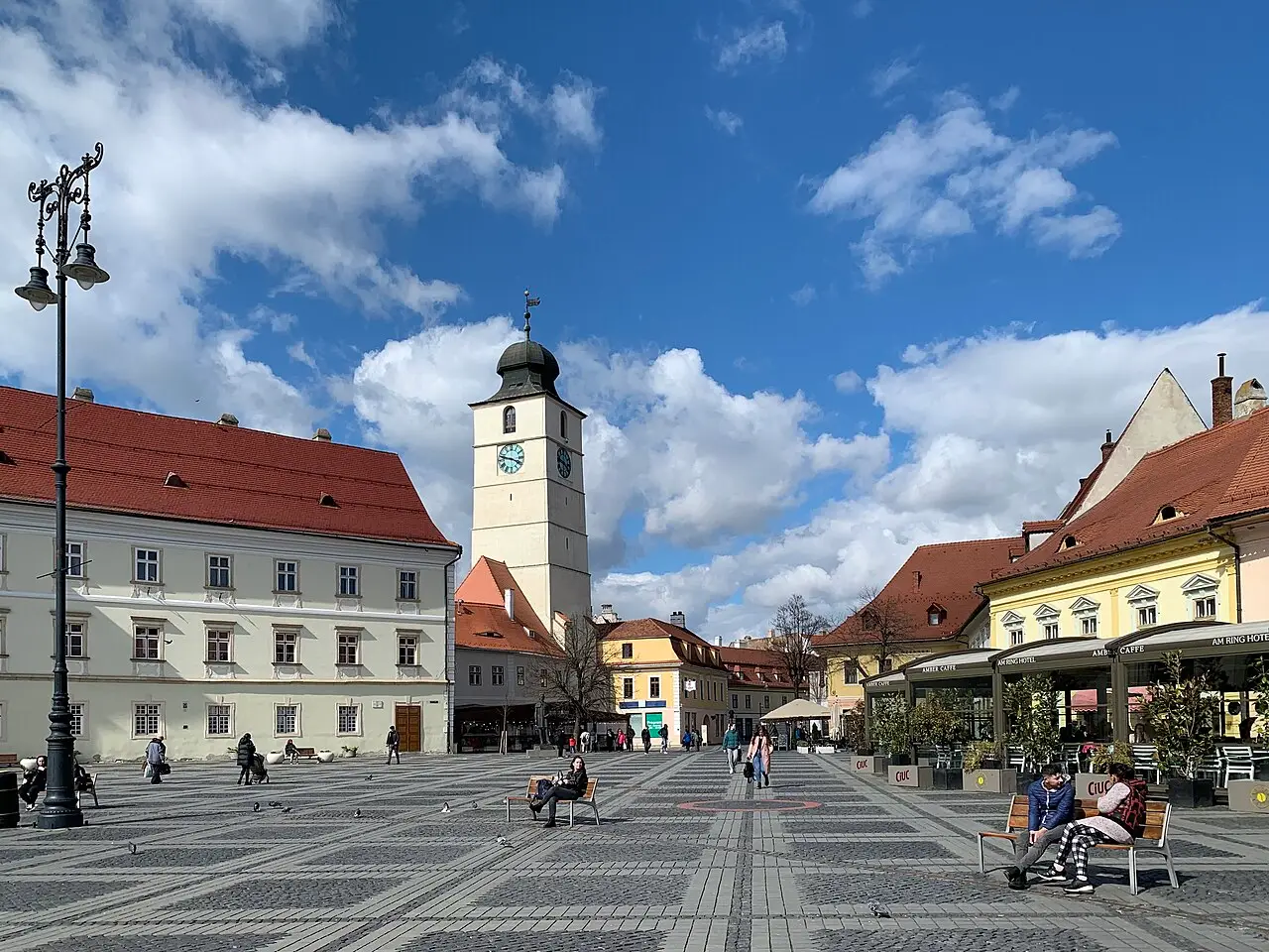 The Large Square of Sibiu ringed by pastel Baroque houses on a clear day, with cafe tables on the cobbles