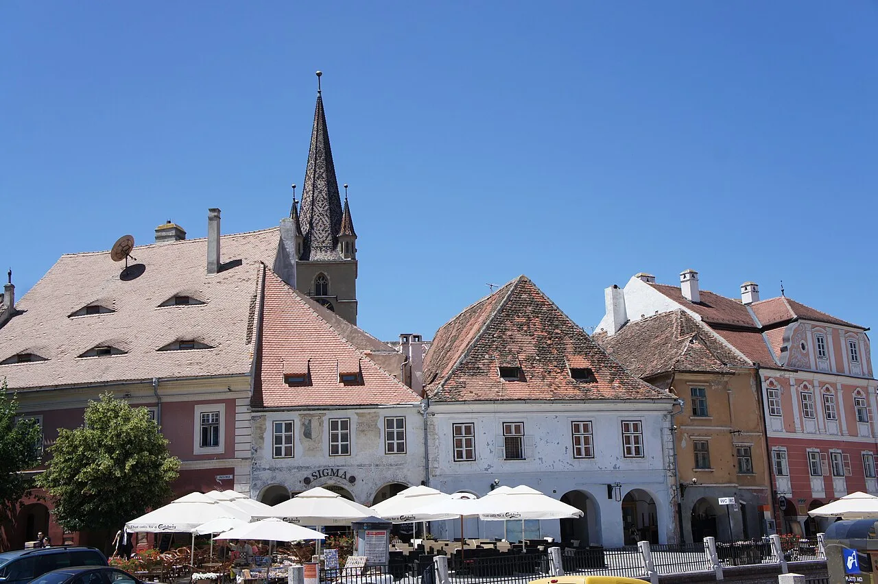 The Small Square of Sibiu with its curving line of arcaded, pastel guild houses under a bright sky