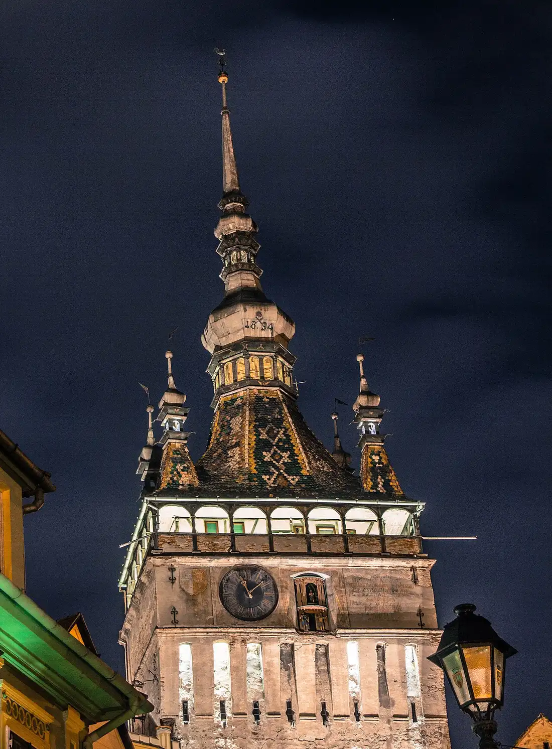 The Clock Tower of Sighisoara from below, its baroque roof and four small corner turrets against a blue sky